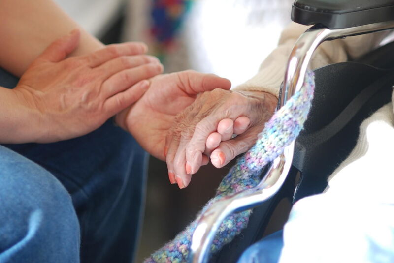 Eine unterstützende Hand hält die Hand einer älteren Person